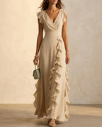 Khaki toned ruffle maxi dress with flutter sleeves and wide pleated waist, worn with heeled sandals