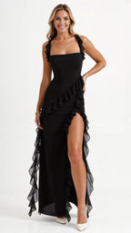 Woman in black ruffled maxi dress with thigh-high slit, squareneck bodice and ruffle shoulder straps, standing front on