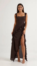 Woman in dark brown ruffled maxi dress with thigh-high slit, standing front on with gold heeled sandals