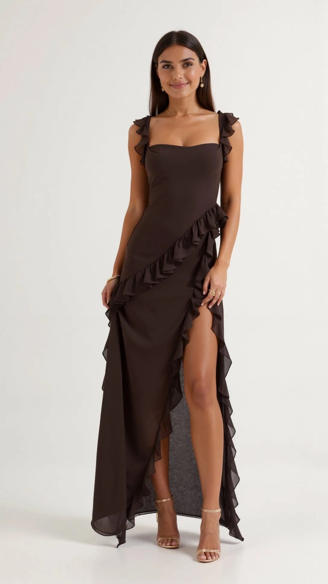 Woman in dark brown ruffled maxi dress with thigh-high slit, standing front on with gold heeled sandals