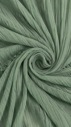 Macro shot of the finely pleated sage green fabric twisted to highlight its soft, crinkled texture and drape