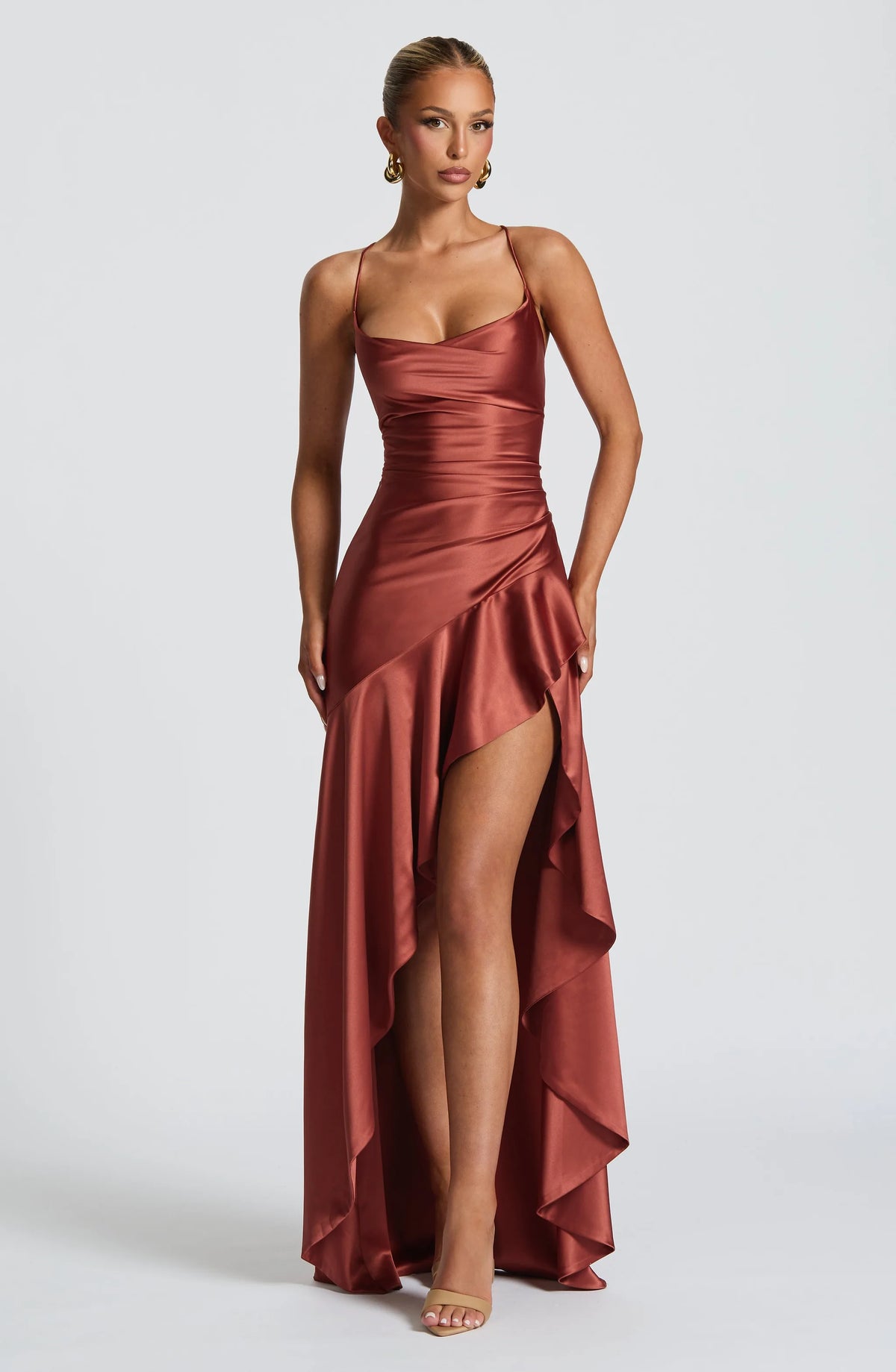 Front view of a model in a brick-red satin maxi dress with cowl neckline and thigh-high slit, hands by her sides