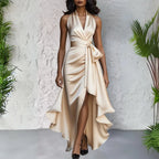 Champagne satin halterneck maxi dress with tie waist detail and ruffled train, shown against a textured wall