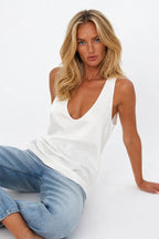 White satin tank top styled with light blue denim jeans, showing the relaxed drape and scoop back racer-style straps