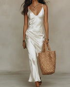Woman walking in a white satin slip maxi dress with a deep V neckline and thin adjustable straps