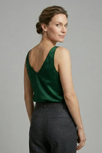 Side profile of a woman wearing a rust orange satin singlet with grey tailored trousers