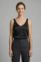 Woman wearing a black satin V-neck singlet with wide straps, styled with grey tailored pants