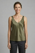 Woman wearing an olive green satin V-neck singlet, front view with grey pants