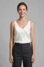Woman wearing an ivory white satin V-neck singlet, front view with grey tailored pants