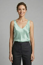 Woman wearing a pale mint green satin V-neck singlet, front view with grey tailored pants