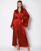 Woman in red satin wrap kimono robe with flared sleeves, tied sash and high leg slit, standing in a studio