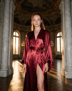 Woman in forest green satin robe standing in a studio, showing the robe's floor-length silhouette