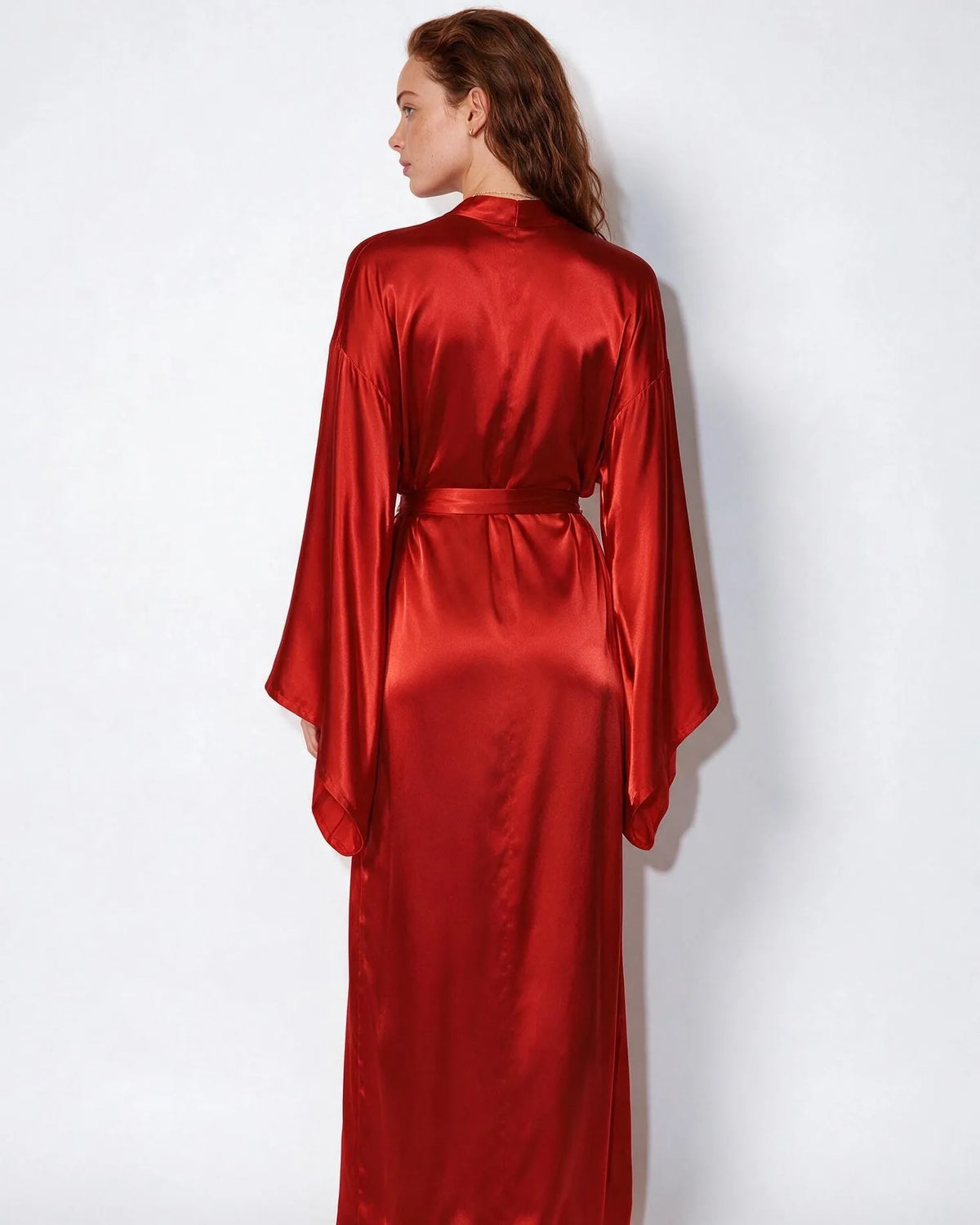 Rear view of woman wearing red satin robe, showing the smooth drape across the back and wide sleeves