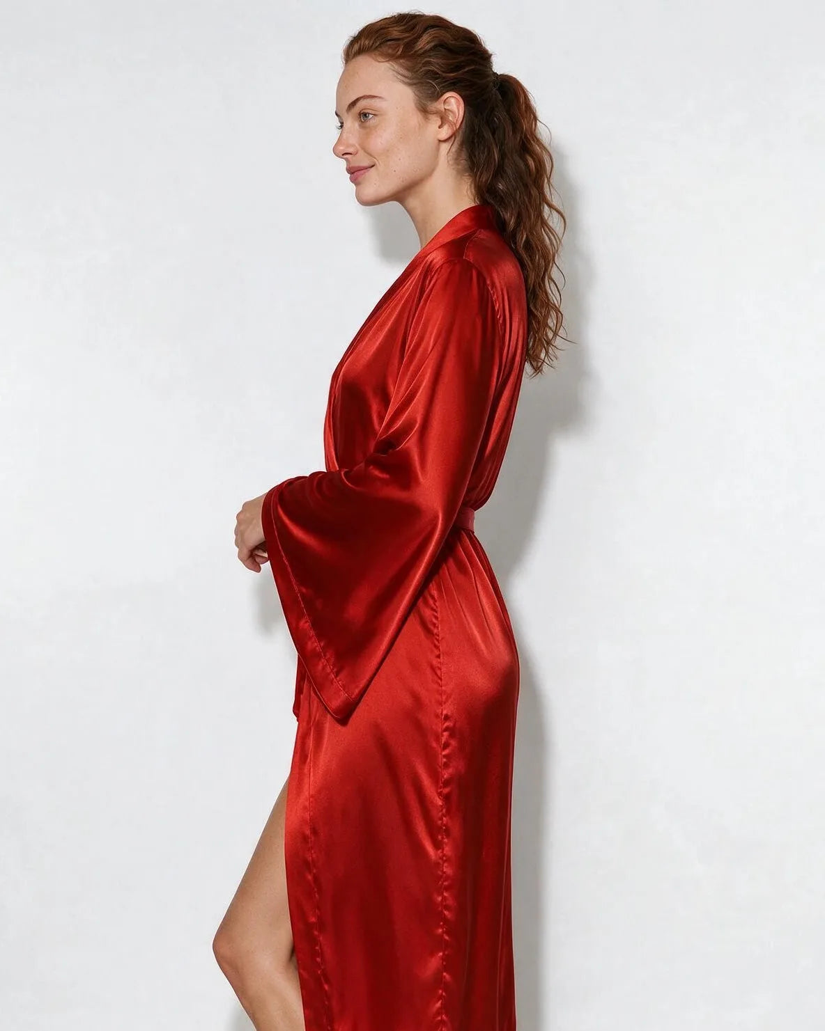 Side profile of woman in red satin robe highlighting the flared kimono sleeve and leg slit