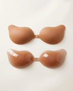 Two tan silicone adhesive bra cups with gold front clasp, shown matte outer surface and glossy inner gel surface