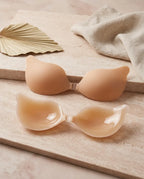Nude adhesive bra cups shown matte-side up and gel-side up on a stone surface beside a woven palm leaf