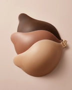 Three adhesive bra cups in deep brown, caramel tan and light nude stacked together showing the gold front clasp closure