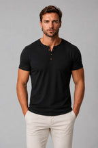 Front view of man wearing black Henley T-shirt with brown buttons, hands in beige pant pockets
