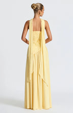 Back view of yellow gown showing lace-up corset detail and long draped scarf panel flowing down the back