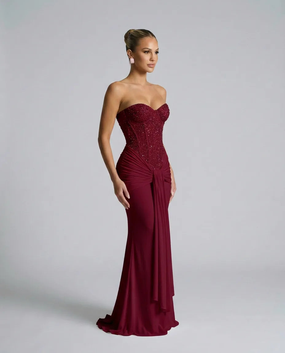 Side angle of the burgundy sequin corset dress highlighting the structured bodice and draped fabric cascading from the waist