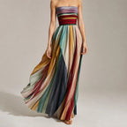 Front view of a strapless multicolour striped maxi dress with a pleated full skirt and ruched bodice, styled with tan heeled sandals