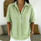 Model wearing a sage green and white striped collared blouse with short sleeves and layered silver necklace