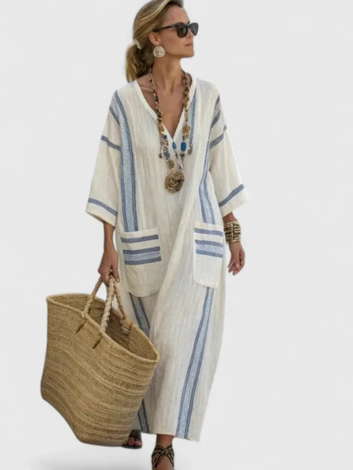 Cream linen maxi dress with soft blue stripes and striped pockets, worn with gold beaded necklaces and a woven tote bag