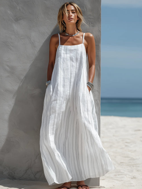 Front view of a woman wearing a flowing white striped maxi dress with square neckline and silver jewellery