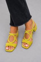 Close-up of yellow suede block-heel sandal with circular cut-out detail worn with cropped black jeans