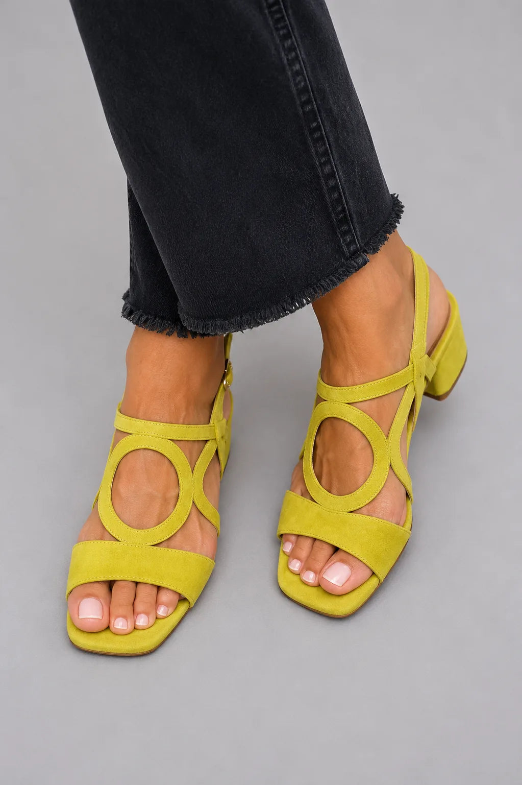 Close-up of yellow suede block-heel sandal with circular cut-out detail worn with cropped black jeans