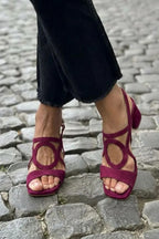 Burgundy suede sandal with circular cut-out and crossover straps, shown on a cobbled street