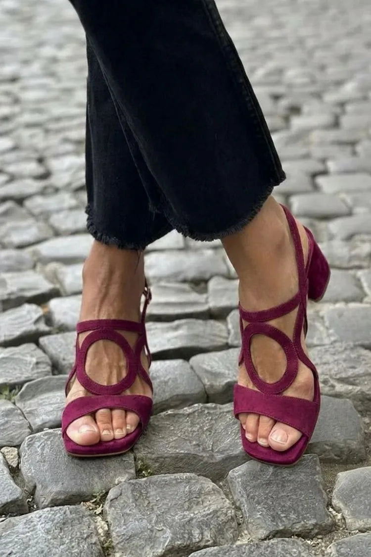 Burgundy suede sandal with circular cut-out and crossover straps, shown on a cobbled street