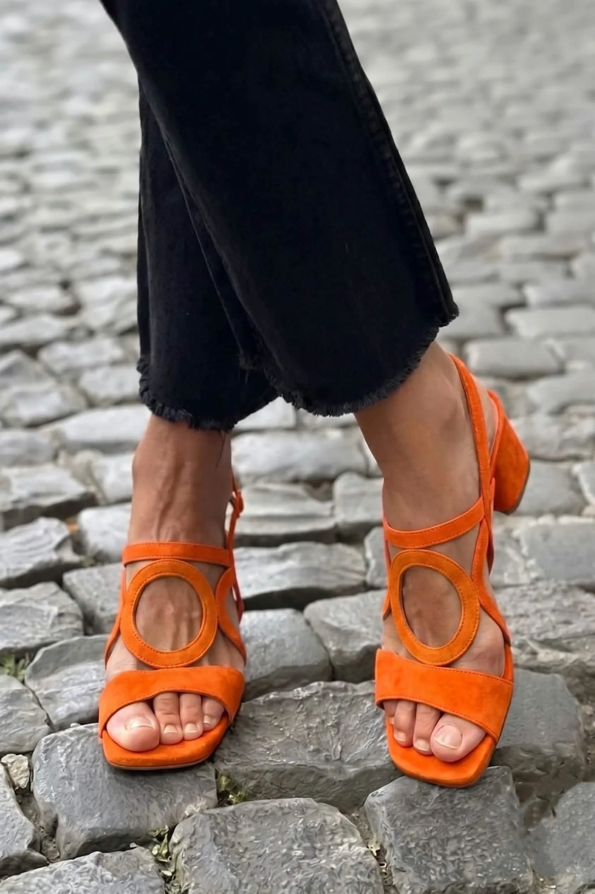 Orange suede sandal with round cut-out detail and chunky low heel, close-up on cobblestones