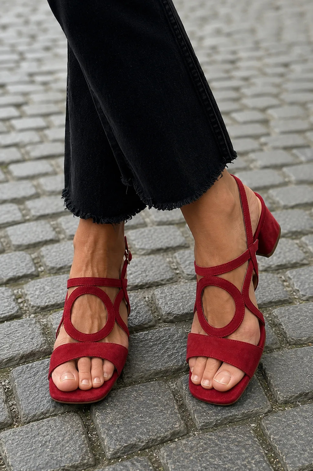 Red suede sandal with circular cut-out and ankle strap, styled with black frayed-hem denim