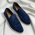 Navy blue suede slip-on loafers with cream soles displayed side by side on white fabric