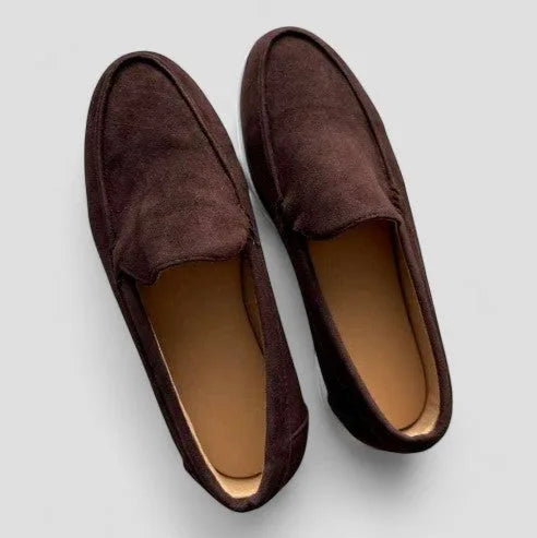 Overhead view of dark brown suede slip-on loafers with tan leather insoles against a grey backdrop