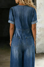 Back view of the blue denim jumpsuit showing puff sleeves, fitted waist seam and twin patch pockets