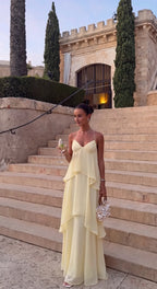 Front view of a butter yellow tiered chiffon maxi dress worn on stone steps with a woven handbag