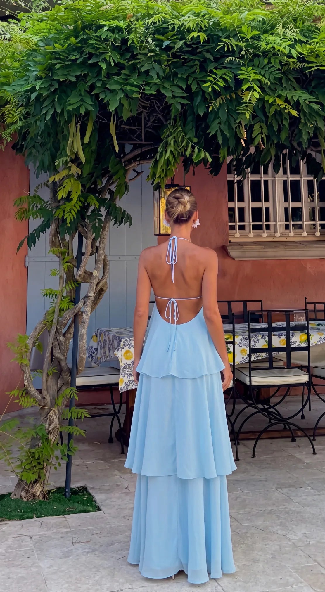 Back view of a baby blue maxi dress showing the open back, halter tie and cascading tiered skirt