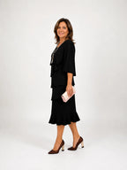 Side profile of a woman walking in a black tiered midi dress with flutter sleeves, pairing it with brown textured heels