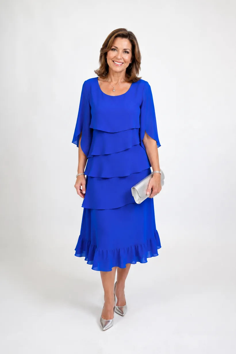 Front view of a woman in a royal blue tiered ruffle midi dress with cape sleeves, styled with a silver clutch and heels