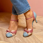 Close-up of pointed-toe heels in light blue and dusty rose with crossover ankle strap and bow detail, worn with cropped jeans