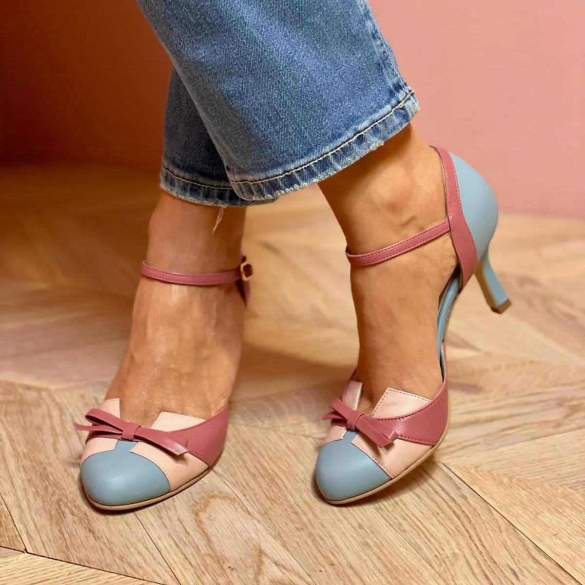 Close-up of pointed-toe heels in light blue and dusty rose with crossover ankle strap and bow detail, worn with cropped jeans
