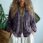 Close-up front view of purple leaf and dragonfly print shirt with green V-neck trim and button closure