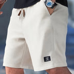 Close-up of white waffle-textured shorts with brown leather drawstring tabs and black woven logo patch