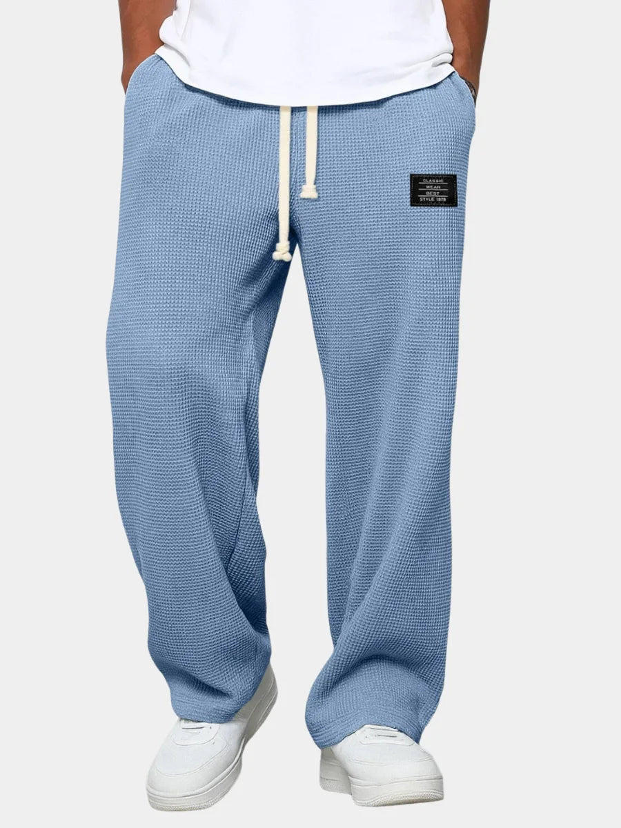 Front view of man wearing sky blue waffle-knit sweatpants with cream drawstring and black logo patch