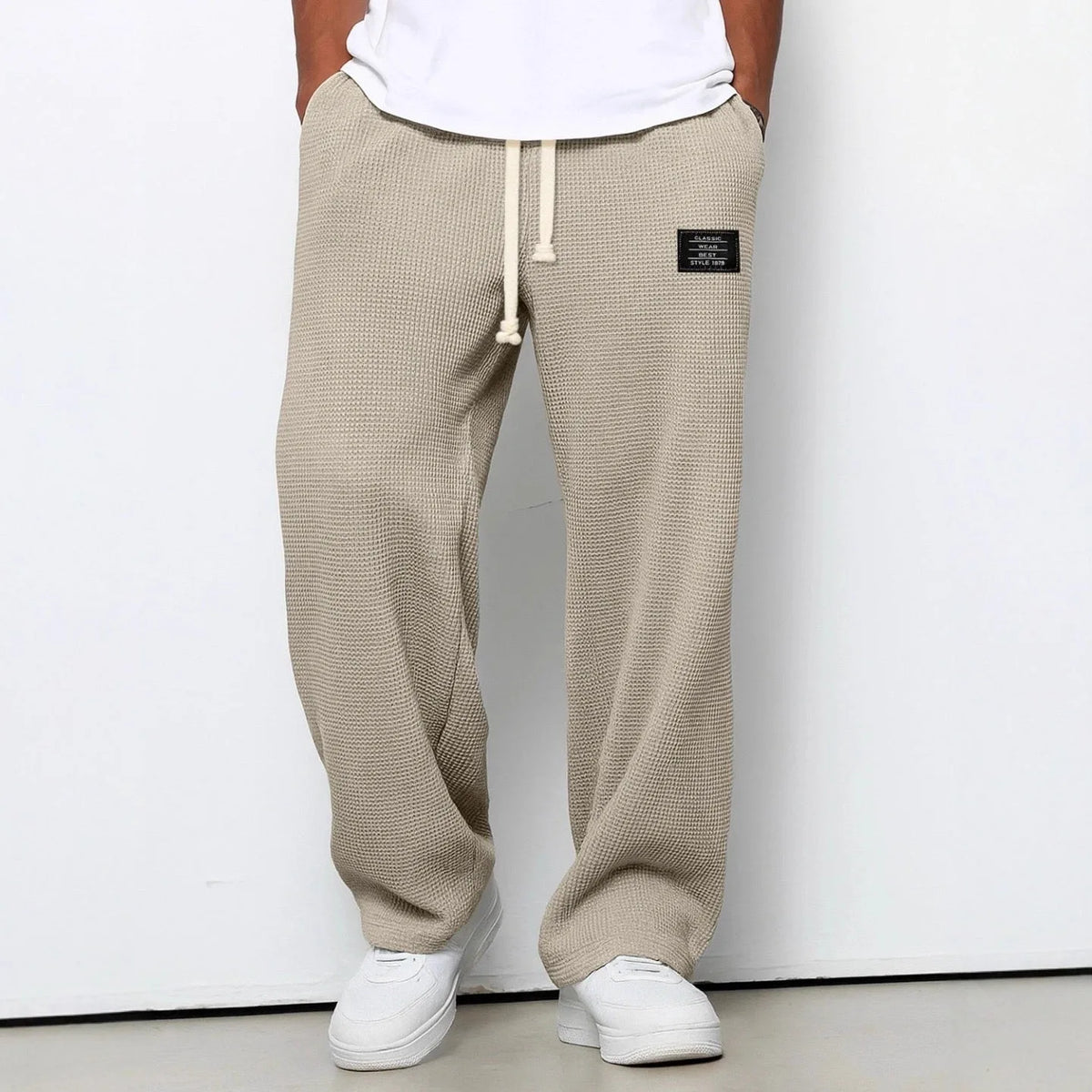 Khaki waffle-knit relaxed fit pants worn with white sneakers, front view against plain wall