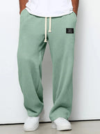Sage green waffle-textured pants shown from front with drawstring waist and logo patch detail