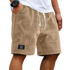 Beige waffle-knit shorts shown on a model from the side, elastic drawstring waist and patch label on hem