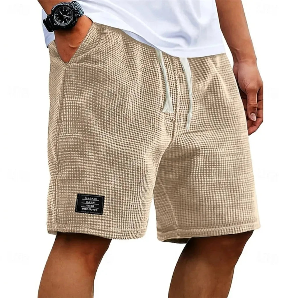 Close-up front angle of beige waffle shorts showing textured fabric weave and fabric patch label on leg